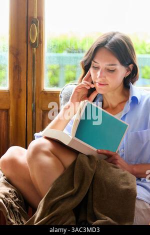 35-jährige Frau zu Hause, liest ein Buch Stockfoto