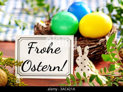 Bayern, Deutschland - 2. April 2025: FOTOMONTAGE, Frohe Ostern Gruß auf einer Grußkarte vor einem Osternest mit bunten Eiern und Dekoration *** FOTOMONTAGE, Frohe Ostern Ostergruß auf einer Grußkarte vor einem Osternest mit bunten Eiern und Dekoration Stockfoto
