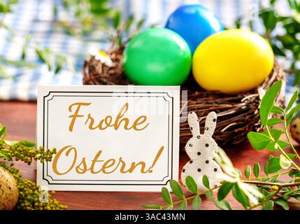 Bayern, Deutschland - 2. April 2025: FOTOMONTAGE, Frohe Ostern Gruß auf einer Grußkarte vor einem Osternest mit bunten Eiern und Dekoration *** FOTOMONTAGE, Frohe Ostern Ostergruß auf einer Grußkarte vor einem Osternest mit bunten Eiern und Dekoration Stockfoto