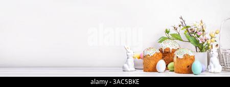 Leckere glasierte Osterkuchen mit Zuckerdekor, farbenfroher Eierkorb, Keramikkaninchen und Frühlingsblumen auf weißem Küchentisch, Kopierraum. Frohe Ostern Stockfoto