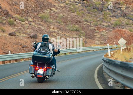 Biker-Paar, das mit dem Hubschrauber durch die Bergstraße fährt. Männliche und weibliche Motorradfahrer, die auf der Autobahn unterwegs sind. Motorradfahrer fahren im Vollgang mit dem Chopper auf kurvenreichen Bergstraßen. Bergige Kulisse Stockfoto