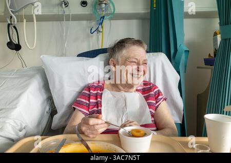 Glückliche ältere Patientin lacht in ihrem NHS Krankenhausbett, England, Großbritannien Stockfoto
