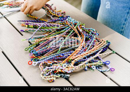 Moskau Russland - 25. August 2023 - Eine Hand greift nach lebendigen gewebten Freundschaftsarmbändern, die auf einem Holztisch angeordnet sind und Vielfalt in Farben und Patten zeigen Stockfoto