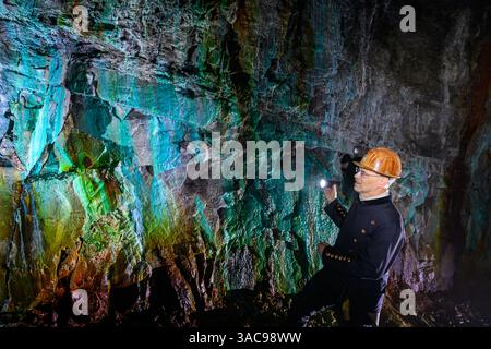 PRODUKTION - 02. April 2025, Sachsen-Anhalt, Sangerhausen: Thomas Wäsche, Leiter des Erlebniszentrums Bergbau Röhrigschacht Wettelrode, steht fast 300 Meter unterirdisch im sogenannten Grünen Gewölbe. Das Sintern wird durch gelöste Mineralien aus dem Kalkstein verursacht. Die Farbpalette reicht von kräftigen Brauntönen bis zu weiß, Grün, Türkis, Blau und Schwarz. Die ersten Bergleute begannen vor 825 Jahren in der Region Mansfeld mit dem Graben nach Kupfererz. Ab 1750 wurde ein intensiver Bergbau durchgeführt. Insgesamt wurden rund 2,6 Millionen Tonnen Kupfer und 14.213 Tonnen Silber aus dem Erz gewonnen Stockfoto