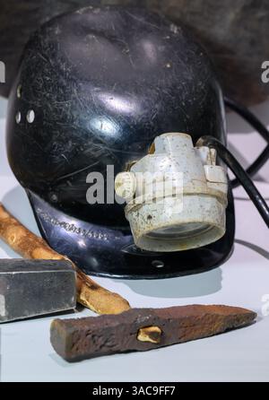 PRODUKTION - 02. April 2025, Sachsen-Anhalt, Sangerhausen: Die Utensilien eines Bergarbeiters, Hammer und Eisen, Fahrerhut und Scheinwerfer sind in der Ausstellung im Erlebniszentrum Bergbau Röhrigschacht Wettelrode zu sehen. Die ersten Bergleute begannen vor 825 Jahren in der Region Mansfeld mit dem Graben nach Kupfererz. Ab 1750 wurde ein intensiver Bergbau durchgeführt. Insgesamt wurden rund 2,6 Millionen Tonnen Kupfer und 14.213 Tonnen Silber aus dem Erz in der Region gewonnen. Bis Dezember werden insgesamt 38 Veranstaltungen an den Beginn der Bergbau- und Hüttenwirtschaft in der Region Mansfeld erinnern. Als Hauptkupfer und si Stockfoto