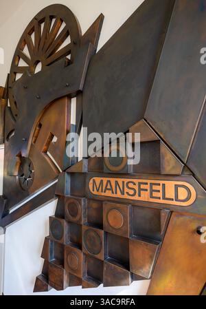 PRODUKTION - 02. April 2025, Sachsen-Anhalt, Hettstedt: Im Mansfeld Museum in Hettstedt ist ein Wandrelief mit der Schrift des Mansfeld-Kombiniers zu sehen. Die ersten Bergleute begannen vor 825 Jahren in der Region Mansfeld mit dem Graben nach Kupfererz. Ab 1750 wurde ein intensiver Bergbau durchgeführt. Insgesamt wurden rund 2,6 Millionen Tonnen Kupfer und 14.213 Tonnen Silber aus dem Erz in der Region gewonnen. Bis Dezember werden insgesamt 38 Veranstaltungen an den Beginn der Bergbau- und Hüttenwirtschaft in der Region Mansfeld erinnern. Als bedeutender Kupfer- und Silberproduzent trug die Region zur wirtschaftlichen Entwicklung bei Stockfoto