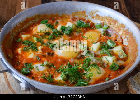 Shakshuka garniert mit frischem Dill und grünen Zwiebeln in einer Pfanne auf Holztisch Stockfoto