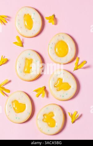 Ostereierkekse mit Zitronenorangenquark, bedeckt mit weißer Glasur und Forsythienblüten auf rosafarbenem Hintergrund. Selektiver Fokus. Stockfoto