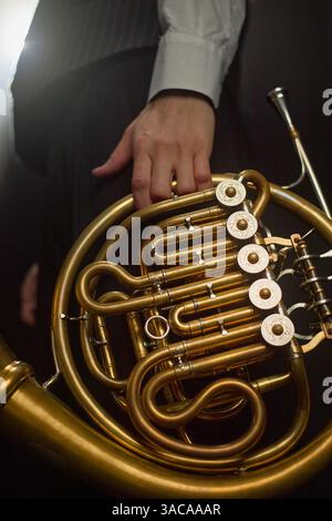 Vertikale Nahaufnahme der Hand eines männlichen Musikers mit glänzendem Horn mit exquisiter Gravur auf den Ventilen, während er sich vor dem Auftritt des Blasinstrumentes auf der Bühne vorbereitete Stockfoto