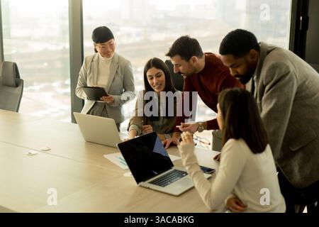 In einem eleganten Büro arbeitet eine Gruppe von Fachleuten an einem Tisch zusammen und teilt Ideen und Erkenntnisse, während sie Notebooks nutzen. Die Atmosphäre ist Stockfoto