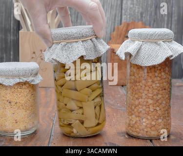Lebensmittelkonservierung im Glasgefäß. Eine Hand, die ein Glas auf einen Holztisch legt. Stockfoto