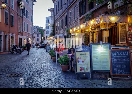 Trastevere in Rom, traditionelle Restaurants und Trattorien am Abend. Rom, Italien - 31. März 2025: Abends in Trastevere, einem typischen Trattoria-Restaurant, das von Touristen in der Stadt besucht wird, mit Tischen im Freien und Menüs auf Plakatwänden im Freien. Beleuchtung und Gasheizung für den Komfort der Gäste. Rom RM Italien Copyright: XGennaroxLeonardix Stockfoto
