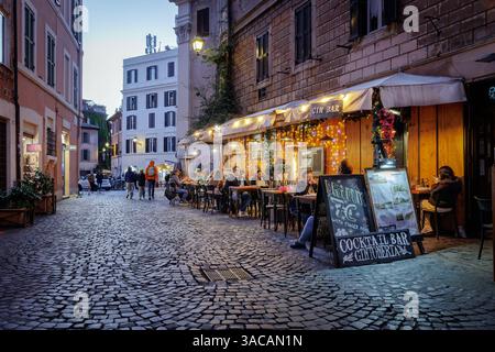 Trastevere in Rom, traditionelle Restaurants und Trattorien am Abend. Rom, Italien - 31. März 2025: Abends in Trastevere, einem typischen Trattoria-Restaurant, das von Touristen in der Stadt besucht wird, mit Tischen im Freien und Menüs auf Plakatwänden im Freien. Beleuchtung und Gasheizung für den Komfort der Gäste. Rom RM Italien Copyright: XGennaroxLeonardix Stockfoto