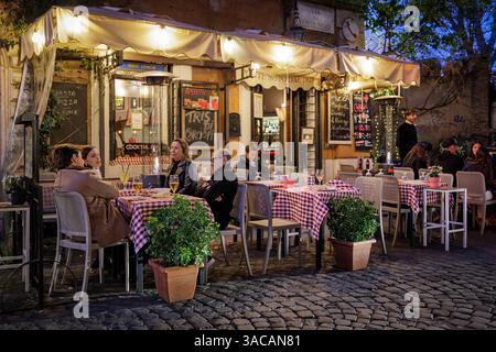 Trastevere in Rom, traditionelle Restaurants und Trattorien am Abend. Rom, Italien - 31. März 2025: Abends in Trastevere, einem typischen Trattoria-Restaurant, das von Touristen in der Stadt besucht wird, mit Tischen im Freien und Menüs auf Plakatwänden im Freien. Beleuchtung und Gasheizung für den Komfort der Gäste. Rom RM Italien Copyright: XGennaroxLeonardix Stockfoto