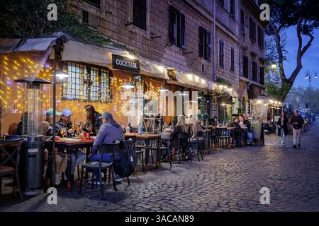 Trastevere in Rom, traditionelle Restaurants und Trattorien am Abend. Rom, Italien - 31. März 2025: Abends in Trastevere, einem typischen Trattoria-Restaurant, das von Touristen in der Stadt besucht wird, mit Tischen im Freien und Menüs auf Plakatwänden im Freien. Beleuchtung und Gasheizung für den Komfort der Gäste. Rom RM Italien Copyright: XGennaroxLeonardix Stockfoto