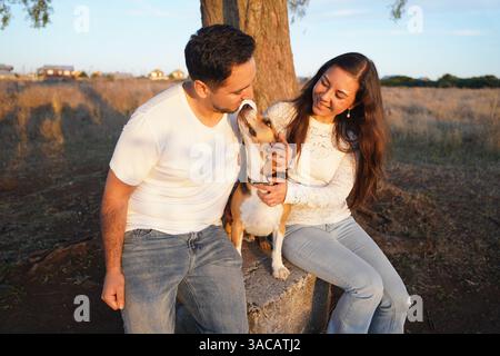 Ein fröhliches und glückliches Paar genießt einen verspielten Moment mit seinem geliebten Hund in einer atemberaubenden Umgebung im Freien Stockfoto