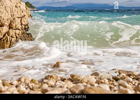 Majestätische, sanfte Wellen, die an einem felsigen Strand brechen. Die Welle platzt an einem steinigen Ufer und bildet einen Sprühnebel. Malerischer Blick auf das Meer. Karte, Banner, tra Stockfoto