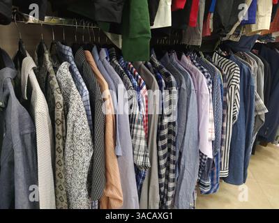 Die Kleidung hing an Kleiderbügeln. Sortiment an Second-Hand-Geschäften. Herrenshirts, die an einem Regal hängen, zum Verkauf an Kunden bereit. Geld sparen in Krisen. Billige s Stockfoto