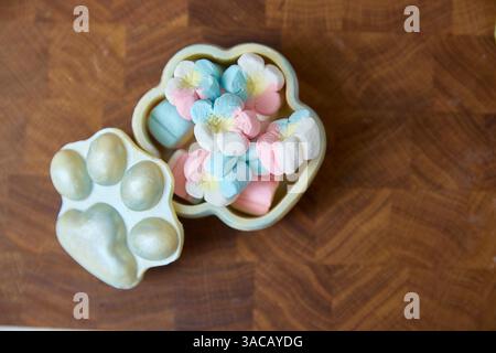 Leuchtende, pastellfarbene Marshmallow-Bonbons platzen sanft aus einer geöffneten, pfotenförmigen, türkisfarbenen Dose und deuten auf Süße, Komfort und spielerische Kindheitserinnerungen hin Stockfoto