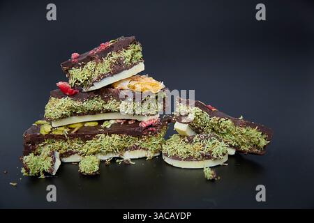 Dubai Schokolade. Luxuriöse dunkle Schokoladenrinde, verziert mit smaragdgrüner Pistazie und rubinroten Früchten, erinnert an Dekadenz und Feier, perfekt für Konfekt Stockfoto