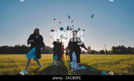 Fröhliche Absolventen in akademischer Kleidung werfen ihre Kappen in die Luft, um den Abschluss ihres Studiums bei Sonnenuntergang zu feiern Stockfoto