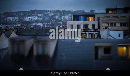 Hochhaus mit Blick auf moderne Dachwohnungen in Brighton in Richtung Terrassenhäuser in der Abenddämmerung. Häuser beleuchtet von innen an einem kalten, bewölkten Abend Stockfoto