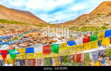 Ladakh, Indien. Weitwinkelblick auf den Bergfluss, der unter Gebetsfahnen aus dem Himalaya-Gebirge ein Tal hinunter rauscht. Stockfoto