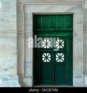 Eine grüne Tür mit geometrischen Glaspaneelen und dekorativen Grilleworks ist in einem kunstvollen Marmorrahmen untergebracht, der neoklassizistische Eleganz veranschaulicht. Stockfoto