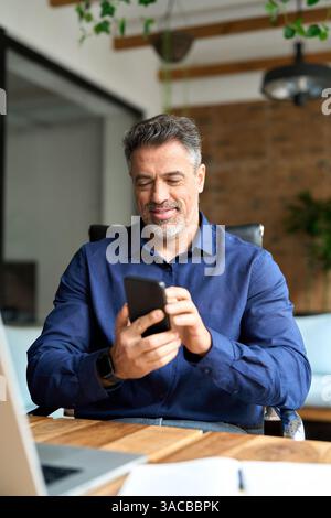 Glücklicher, reifer Geschäftsmann, Unternehmensleiter, der im Büro ein Handy benutzt. Stockfoto