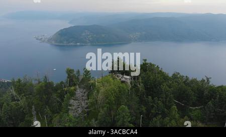 Der Baikalsee am Abend. Blick aus der Vogelperspektive auf eine hölzerne Aussichtsplattform, eingebettet in einen Wald, mit Blick auf die weite Weite des baikalsees und die Ferne Stockfoto