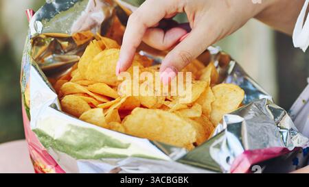 Frau, die Kartoffelchips aus einem Folienbeutel packt und ungesunde Essgewohnheiten und Snacks hervorhebt Stockfoto