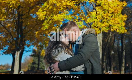 Liebevolles Paar küsst sich unter goldenen Herbstblättern und fängt während der Herbstsaison intime emotionale Verbindungen in malerischer Parklandschaft ein Stockfoto