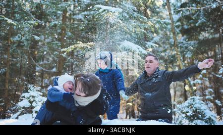 Glückliche Familie, die gemeinsam in einem verschneiten Winterwald spielt, freudig Schnee wirft und den Zauber der weihnachtsfeiertage feiert Stockfoto