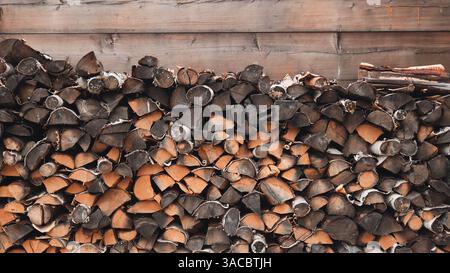 Veraltetes Brennholz, das dicht gegen verwitterte Holzwände stapelt und eine rustikale Textur schafft Stockfoto