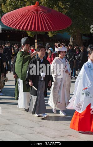 Formelle Hochzeitsprozession mit Braut, Bräutigam und Familie, eingeläutet von Mitgliedern des Shinto-Schreins mit miko und rotem Regenschirm im Meiji Jingu in Tokio, Japan. Stockfoto