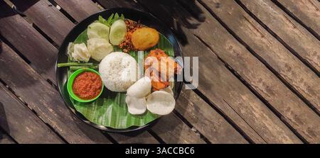 Lebendige Platte mit traditionellem indonesischem Lalapan, mit Reis, gebratenem Huhn, frischem Gemüse und Sambal (Chili-Sauce), mit einem köstlichen Kamm Stockfoto