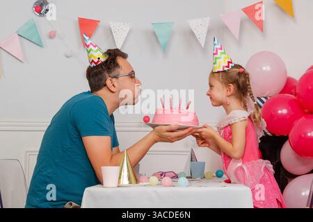 Dad mit seiner Tochter bläst Kerzen auf Geburtstagskuchen aus Stockfoto