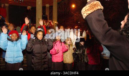11. Dezember 2004 - Cincinnati, Ohio, USA - Regie: Della Enns,(R), zwanzig OTR Nachbarschaftskinder, Mitglieder des After-School-Programms „Art and Soul on Vine“, singen Weihnachtslieder, während sie am Luminaria Harmony of Light-Programm im Washington Park teilnehmen, das 2000 nach den Cincinnati-Unruhen von Thomas Courtney gegründet wurde, für die Bewohner des Rheins. (Bild: © Ken Stewart/ZUMA Press) Stockfoto