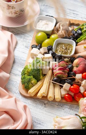Lebendige vegane Käseplatten Flat Lay – farbenfroher Aufstrich auf Pflanzenbasis mit Obst, Gemüse, Nüssen, Brot und Blumen Stockfoto