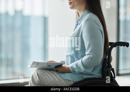 Zugeschnittenes Seitenporträt einer jungen Geschäftsfrau im Rollstuhl, die ein Heft hält, während sie eine Rede hält oder an einer Konferenz teilnimmt, Kopierraum Stockfoto