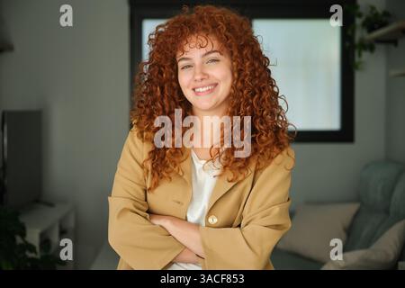 Selbstbewusste junge Geschäftsfrau lächelt mit gekreuzten Armen im Heimbüro Stockfoto