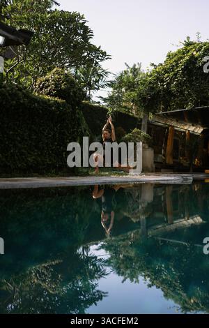 Junge Frau, die Yoga am Pool praktiziert Stockfoto