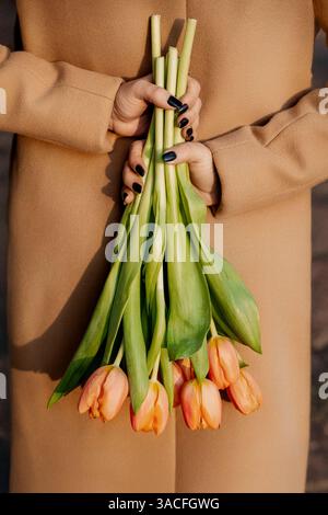 Hände, die Tulpenstrauß in beigem Mantel halten Stockfoto