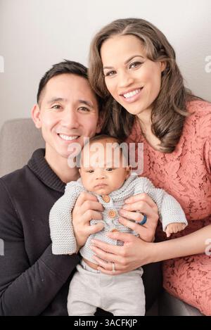 Glückliche Eltern kuscheln ihr Baby für ein süßes Familienporträt zu Hause Stockfoto