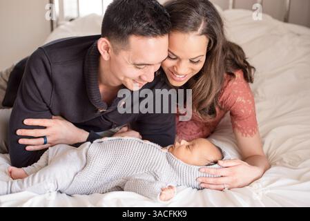 Liebevolle Eltern blicken das schlafende Baby auf einem gemütlichen weißen Bett Stockfoto