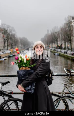 Frau, die Tulpen in der Amsterdamer Kanalbrücke hält Stockfoto