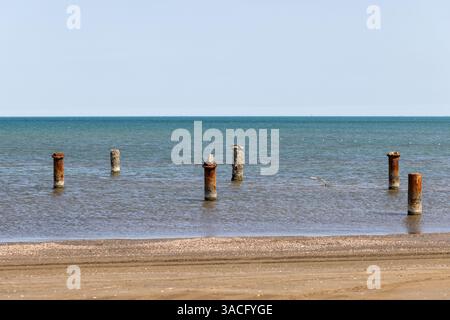 Landschaftsfoto an der kaspischen Küste an einem sonnigen Tag, Aserbaidschan. Verwitterte, rostige Pfosten erheben sich aus dem flachen Meer und verkörpern die Geschichte inmitten des Meeres Stockfoto
