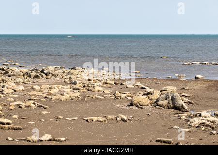 Eine ruhige Küstenszene mit einer felsigen Küste und einem ruhigen, weitläufigen Ozeanhorizont unter hellem Himmel. Landschaft mit der Küste des Kaspischen Meeres, Buzov Stockfoto