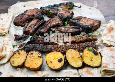 Barbecue mit gegrilltem Fleisch und Schaschlik. Gegrillte Lammrippchen, Kebab, Kartoffeln und Pita-Brot auf Holzbrett. Restaurant Essen, Schweinegrillen, bbq Stockfoto