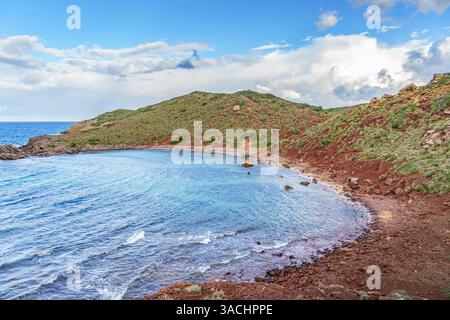 Faszinierender Blick aus der Vogelperspektive auf Cala Rotja, Menorca, wo türkisfarbenes Wasser sanft die einzigartige rötliche Küste küssen und eine ruhige und abgeschiedene Zuflucht bieten Stockfoto